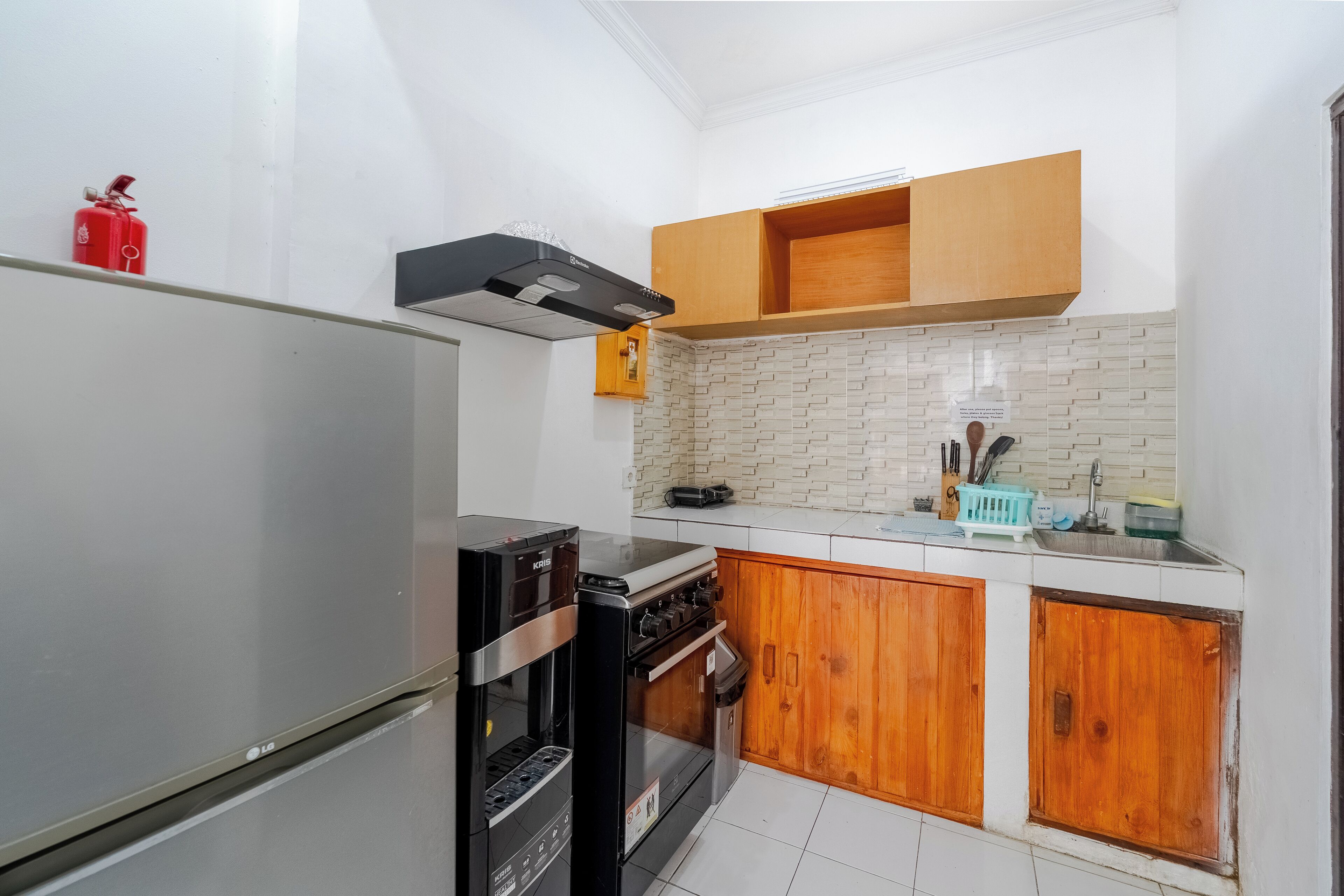 Een kleine keuken met een koelkast, fornuis, oven, houten kastjes en een betegelde achterwand.