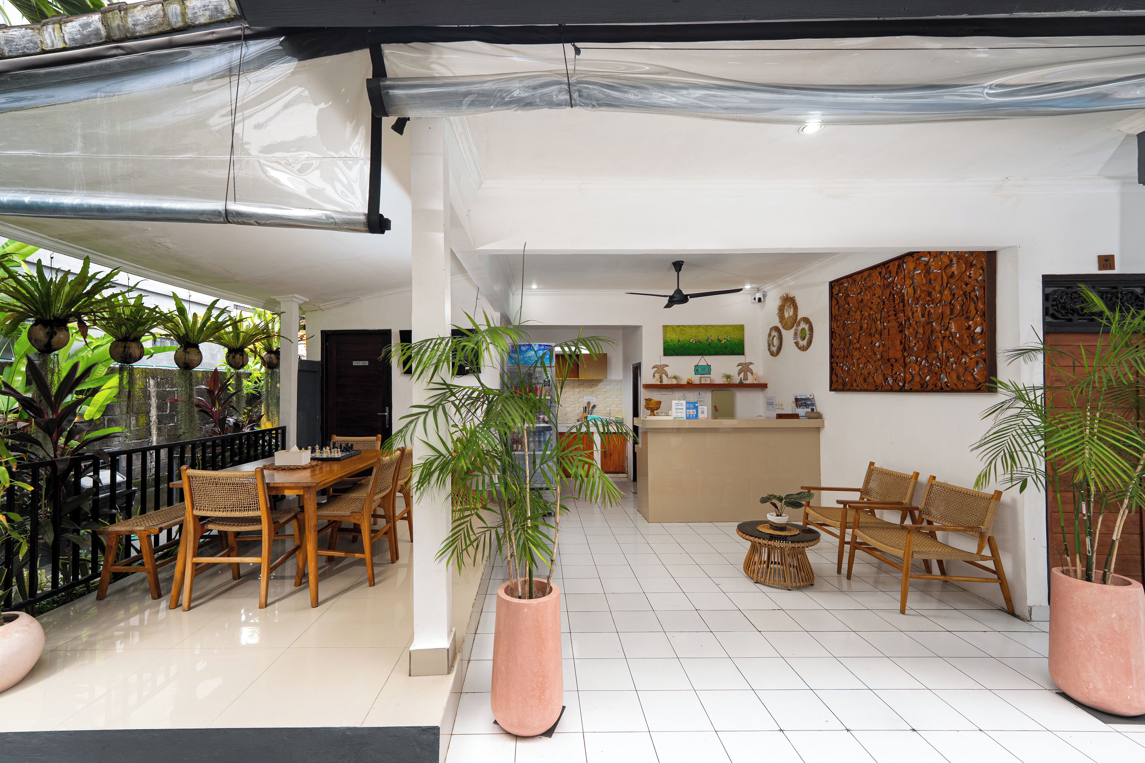 A spacious indoor area with a wooden dining table and chairs, a seating area with a sofa and armchairs, and several potted plants.