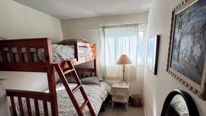 Un dormitorio compacto con una cama litera, una mesita de noche pequeña, una lámpara y un cuadro en la pared.