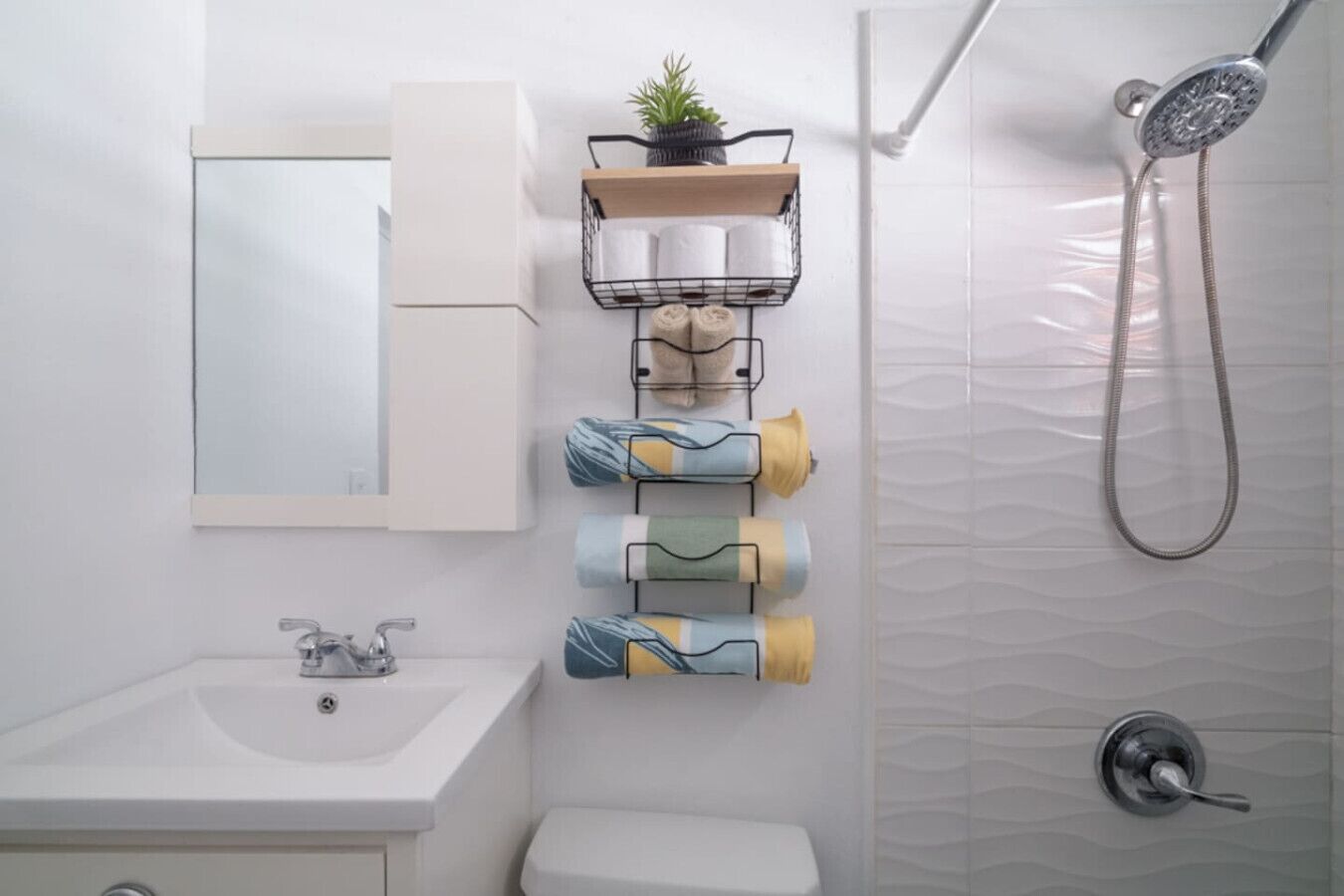 A bathroom with a sink, a mirror, a towel rack with towels, a shower, and a toilet.