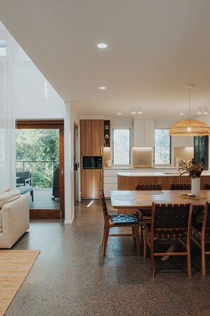 A modern kitchen with a dining area, wooden cabinets, and a large window. - Copacabana at The Sebel (Twin Waters)