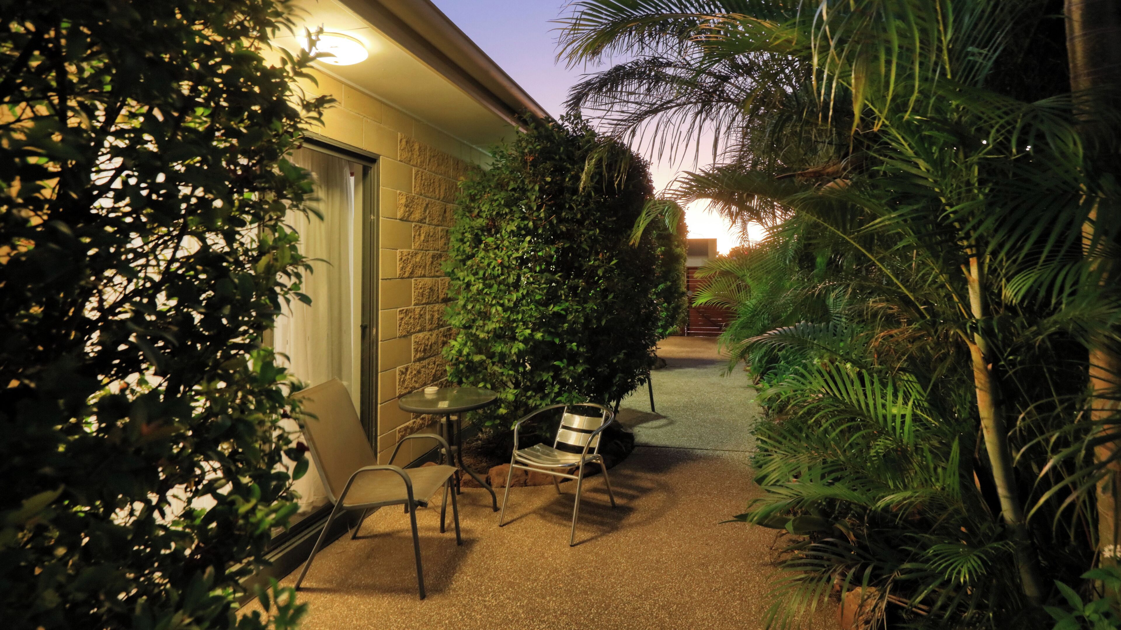 An outdoor patio area with a table and chairs, surrounded by greenery and a brick wall.