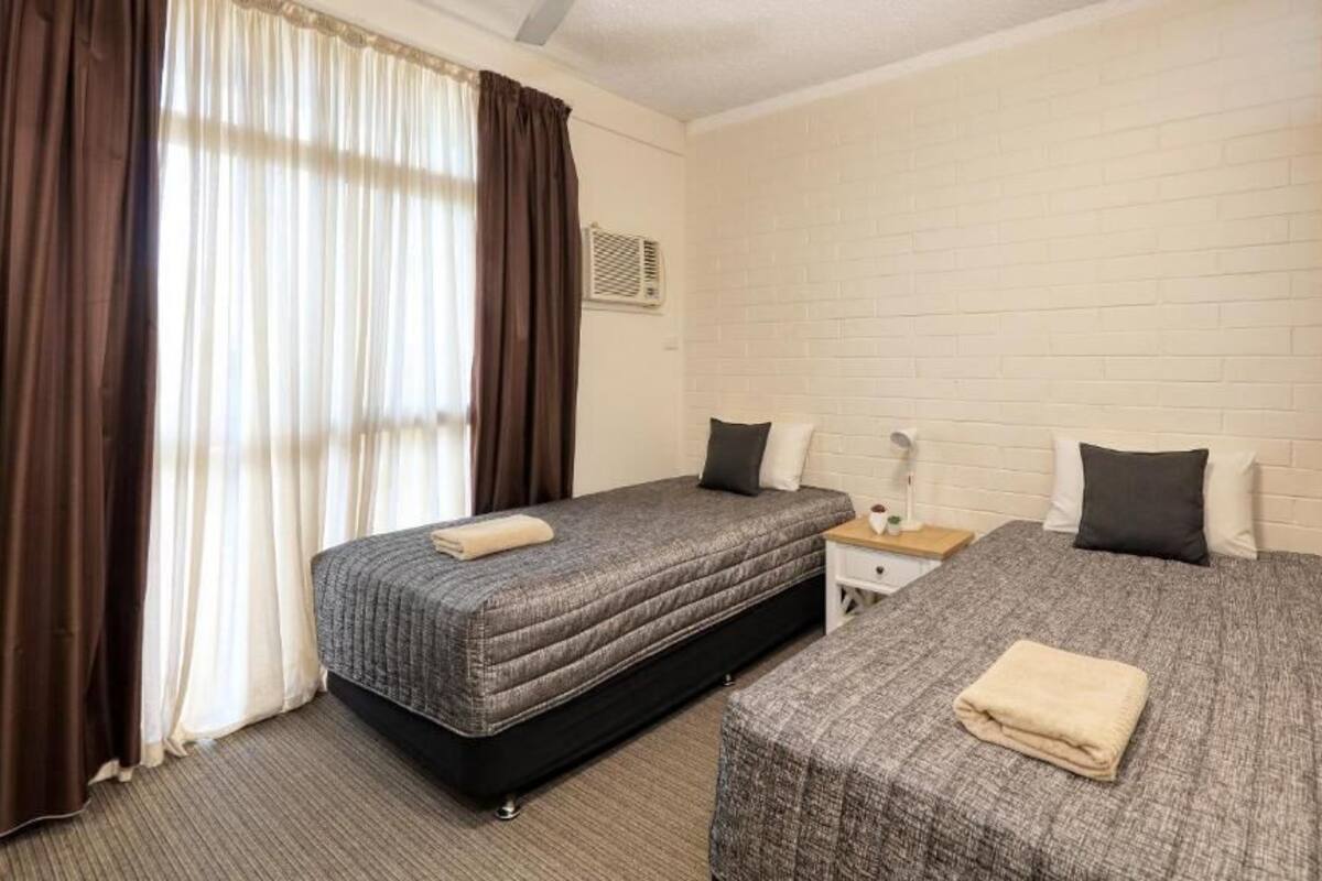 A room with two beds, a nightstand, a lamp, and a window with curtains.