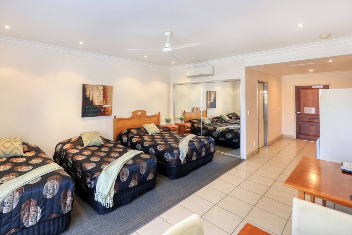 A hotel room with three beds, a desk, a chair, a ceiling fan, and a mirror.