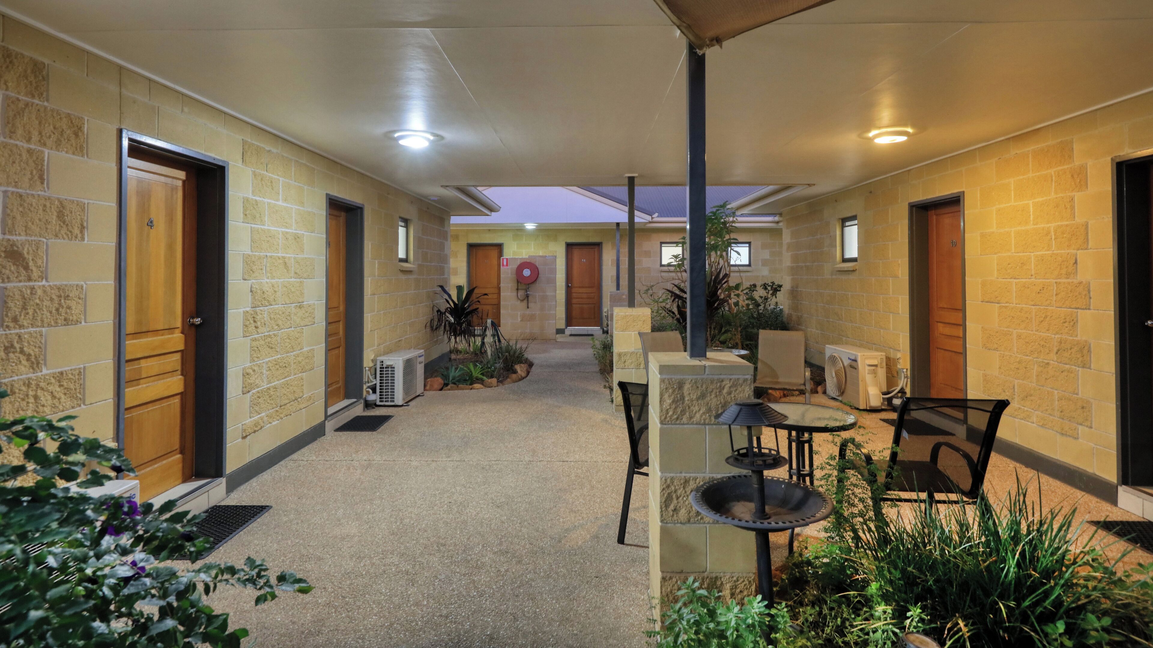 Un pasillo con puertas, unidades de aire acondicionado y zona de estar exterior con plantas.
