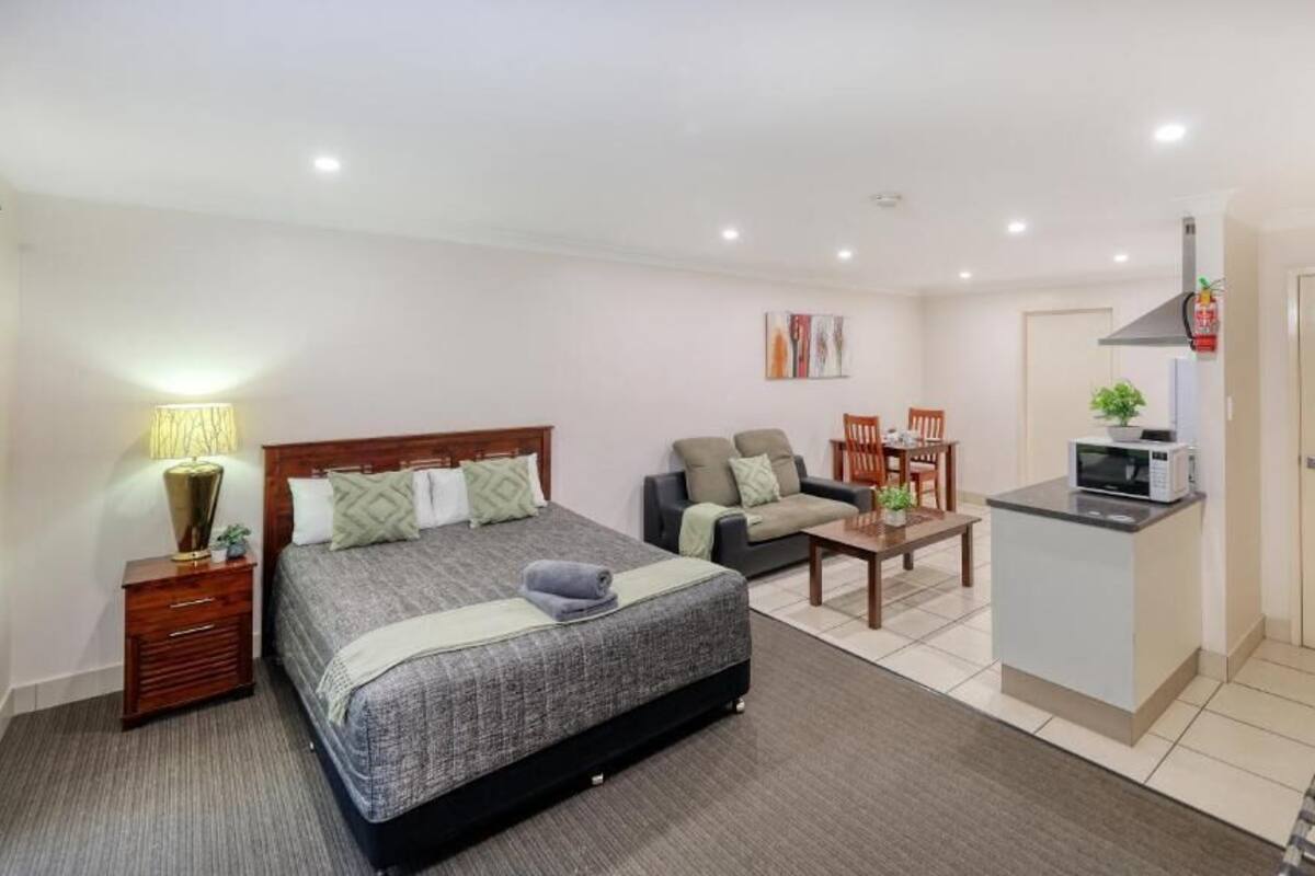 A hotel room with a bed, a sofa, a small dining table, a microwave, and a cabinet.