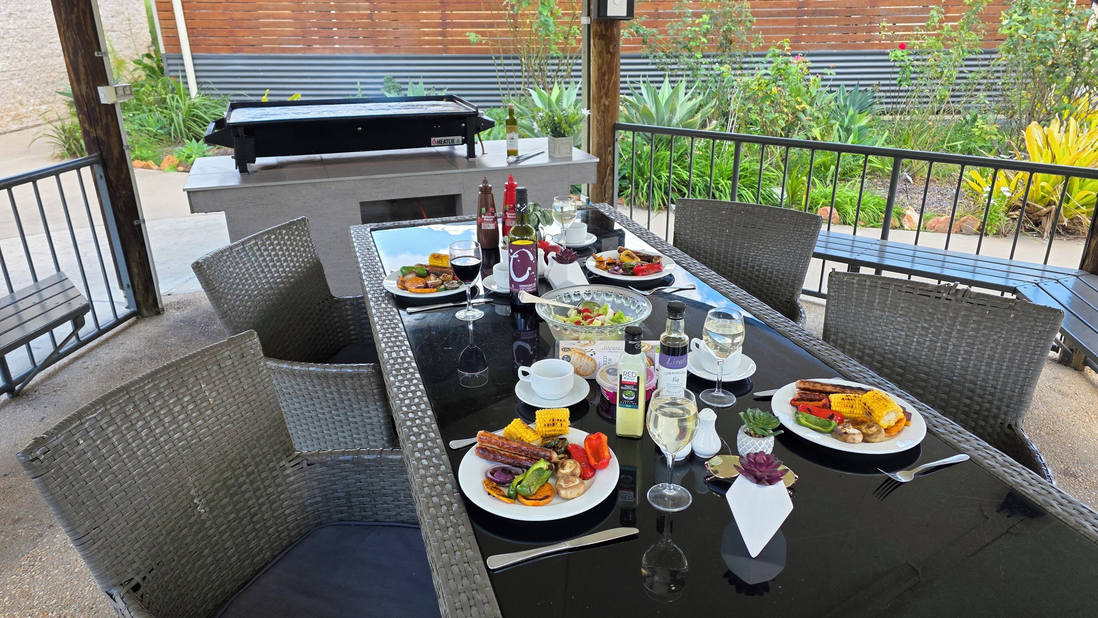 An outdoor dining area with wicker chairs, a glass-top table, and a barbecue grill.