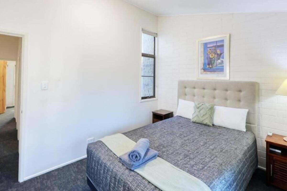 A bedroom with a large bed, a headboard, a nightstand, a lamp, and a painting on the wall.