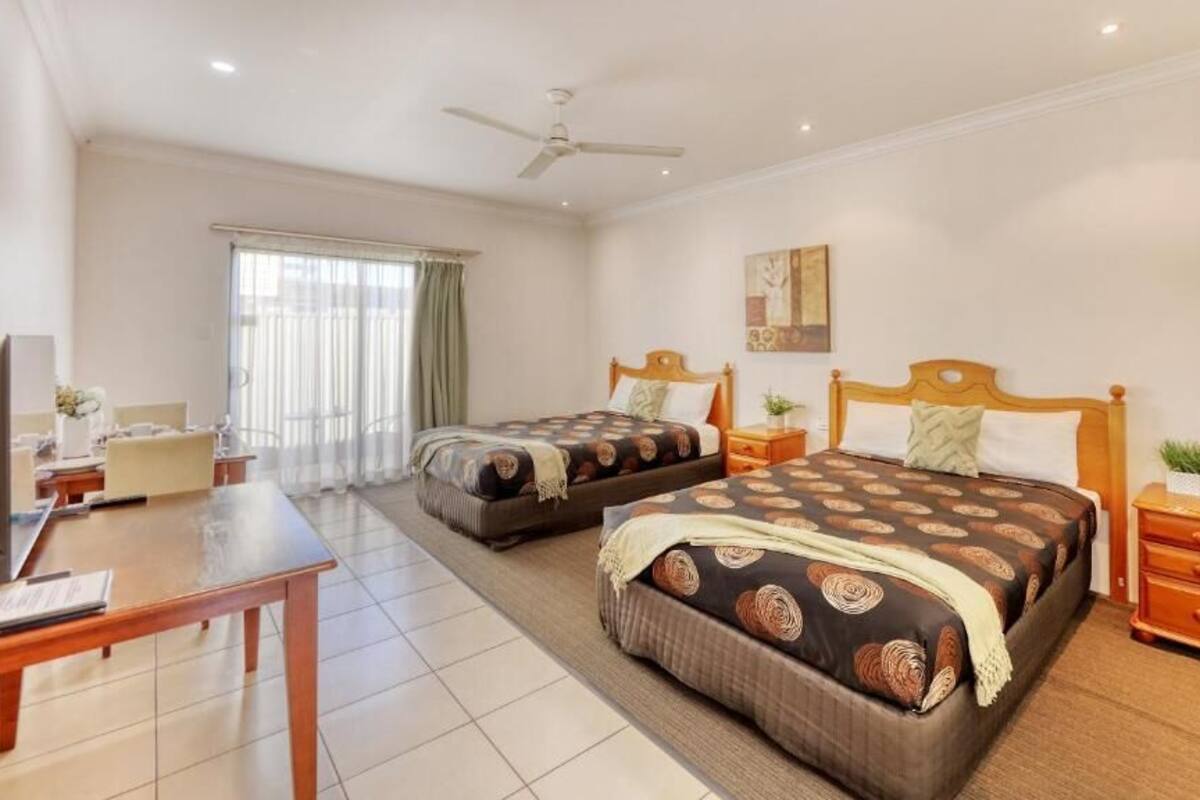 A hotel room with two beds, a desk, a chair, a TV, and a window with curtains.