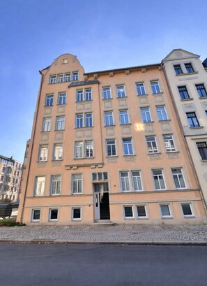 A multi-story building with a symmetrical facade, a central entrance, and a series of windows on each floor. - Comfortable 3-room apartment + kitchen + bathroom + balcony (Chemnitz)