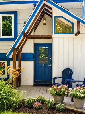 Een huis met een blauwe deur, een houten veranda en bloempotten.