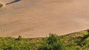 Un parcours de golf avec des bunkers de sable, un obstacle d’eau et des collines boisées en arrière-plan.