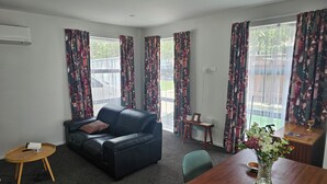Ein Wohnzimmer mit einer schwarzen Ledersofa, einem Holztisch, einem Esstisch mit Blumenvase und einem kleinen Beistelltisch.