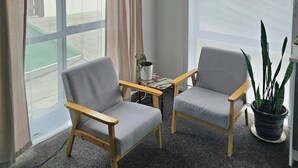 Ein Zimmer mit zwei grauen Sesseln, einem kleinen Tisch und einem Blumentopf.