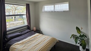 Ein Schlafzimmer mit Bett, einem Fenster mit Vorhängen, einem Nachttisch mit Lampe und einer Topfpflanze.