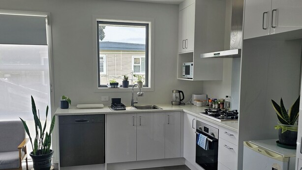 Eine moderne Küche mit weißen Schränken, einer eingebauten Mikrowelle und einem Herd. Ein Fenster sorgt für natürliches Licht und bietet einen Blick ins Freie.