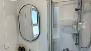 Ein modernes Badezimmer mit einer Duschkabine aus Glas, einem runden Spiegel und einem weißen Waschtisch.