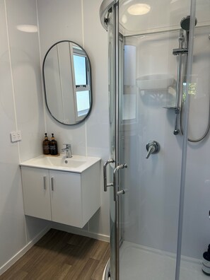 A modern bathroom with a glass-enclosed shower, a round mirror, and a white vanity with a sink. - Magic on Manuka - Relax & Unwind (Mangakino)