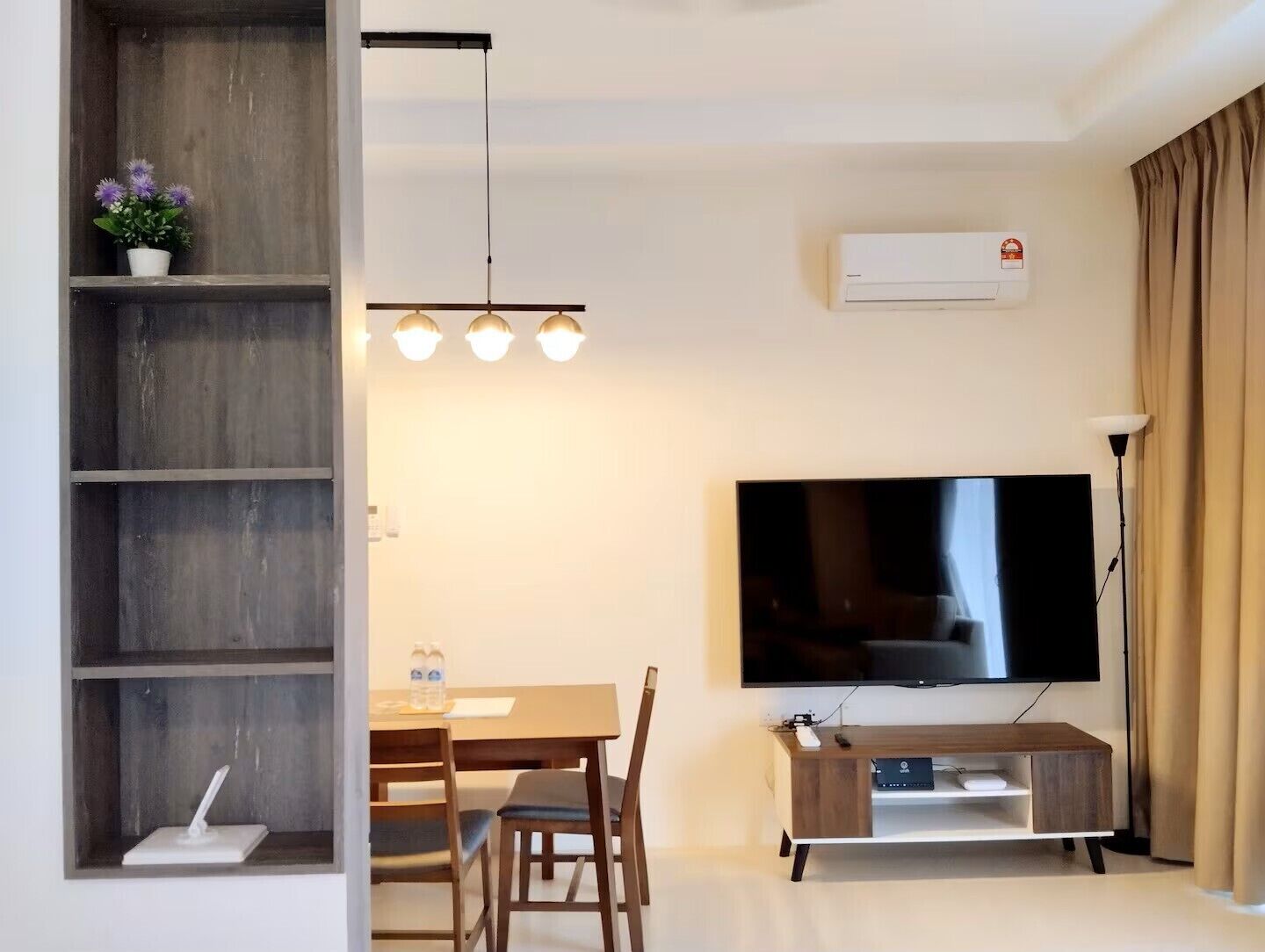 A modern living room with a flat-screen TV, wooden furniture, and a ceiling light fixture.