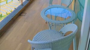 Un balcón con sillones de mimbre y una mesa de vidrio, con vistas a un paisaje urbano con edificios y un río.