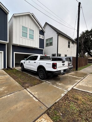 Ein weißer Pritschenwagen steht in einer Einfahrt vor einem zweistöckigen Haus mit Garage.