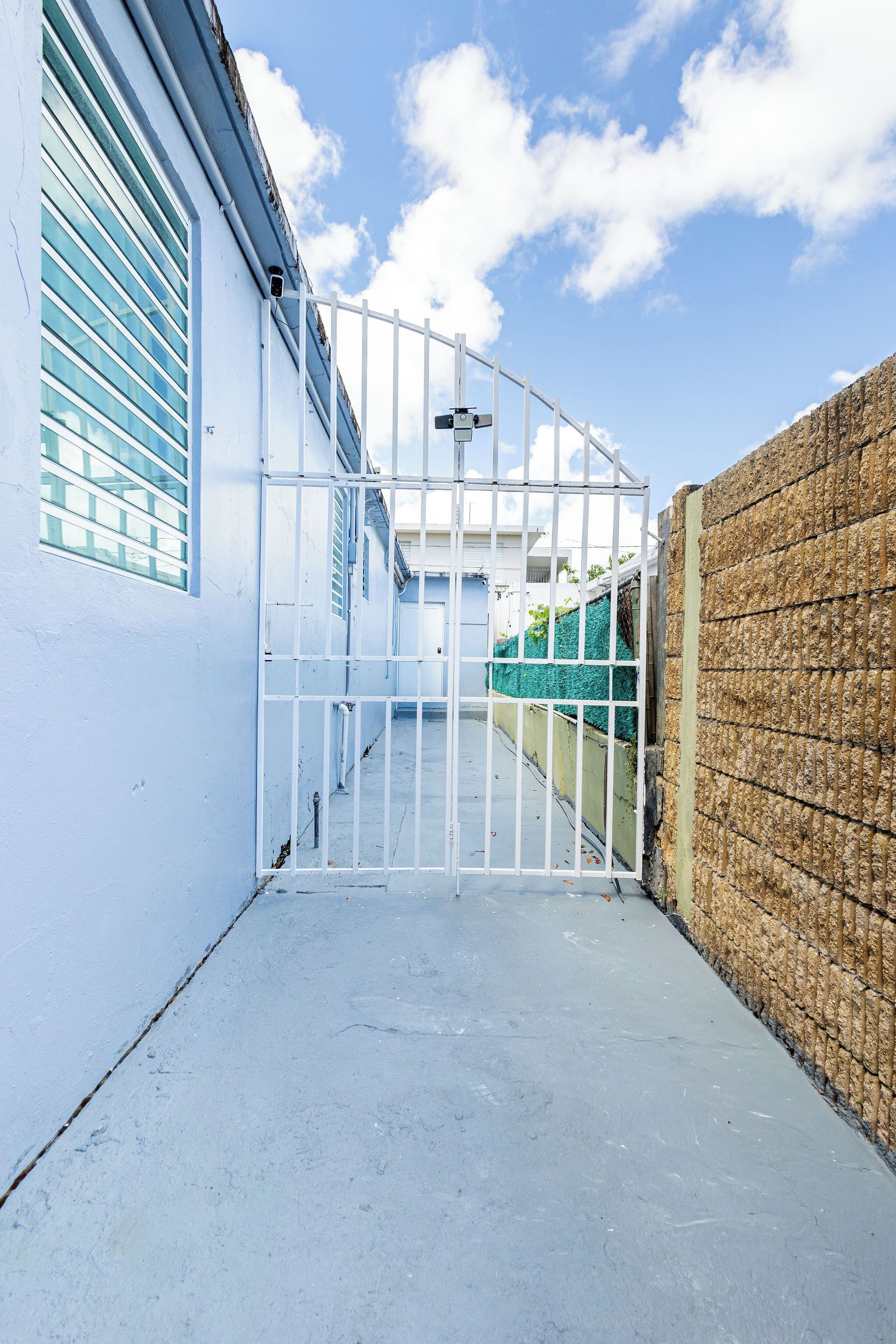 A gated entrance with a concrete pathway leading to a building with a blue exterior and a white fence.