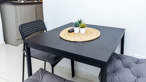 Une table à manger moderne, agrémentée d’un set de table en fibres tressées, de deux petites plantes en pot et d’une télécommande.