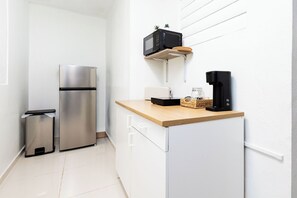 A compact kitchen with a stainless steel refrigerator, a microwave, a coffee maker, and a small trash bin. - Central San Juan 2BR Parking Near Airport (san juan)