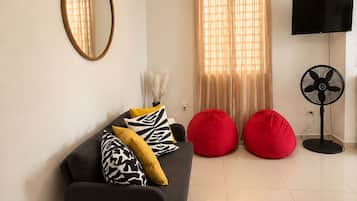 A modern living room with a sofa, red bean bag chairs, a flat-screen TV, and a ceiling fan.