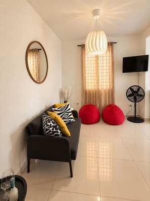 A modern living room with a sofa, red bean bag chairs, a flat-screen TV, and a ceiling fan. - Central San Juan 2BR Parking Near Airport (san juan)