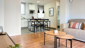 Un salon moderne avec un plancher en bois, une table basse ronde et un canapé agrémenté de coussins à motifs. On aperçoit à l’arrière-plan un coin repas avec une table et des chaises.
