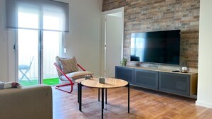 Un salon moderne avec un mur en briques, un téléviseur à écran plat, un fauteuil rouge, une table basse en bois et un canapé.