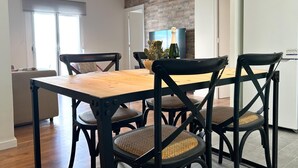 Un coin repas avec une table en bois et des chaises noires à assise tressée. Deux lampes suspendues noires sont placées au-dessus de la table.