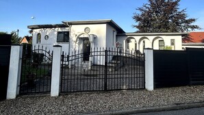 Un bâtiment à deux étages, doté d’une entrée fermée par un portail, d’une allée et d’un arbre en arrière-plan.