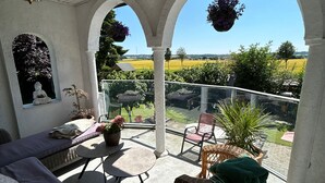 Une terrasse couverte avec un canapé, des chaises, une table, des jardinières suspendues et une vue sur un paysage verdoyant.