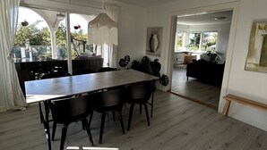 Une salle à manger spacieuse, avec une longue table et des chaises, un lustre et une vue sur l’extérieur.
