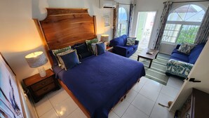 Een slaapkamer met een groot bed, een houten hoofdbord, een nachtkastje, een lamp, een blauwe bank en uitzicht op het landschap door een raam.