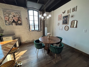 Uma sala de jantar com mesa de madeira, cadeiras estofadas em verde, um vaso com flores e um candelabro.