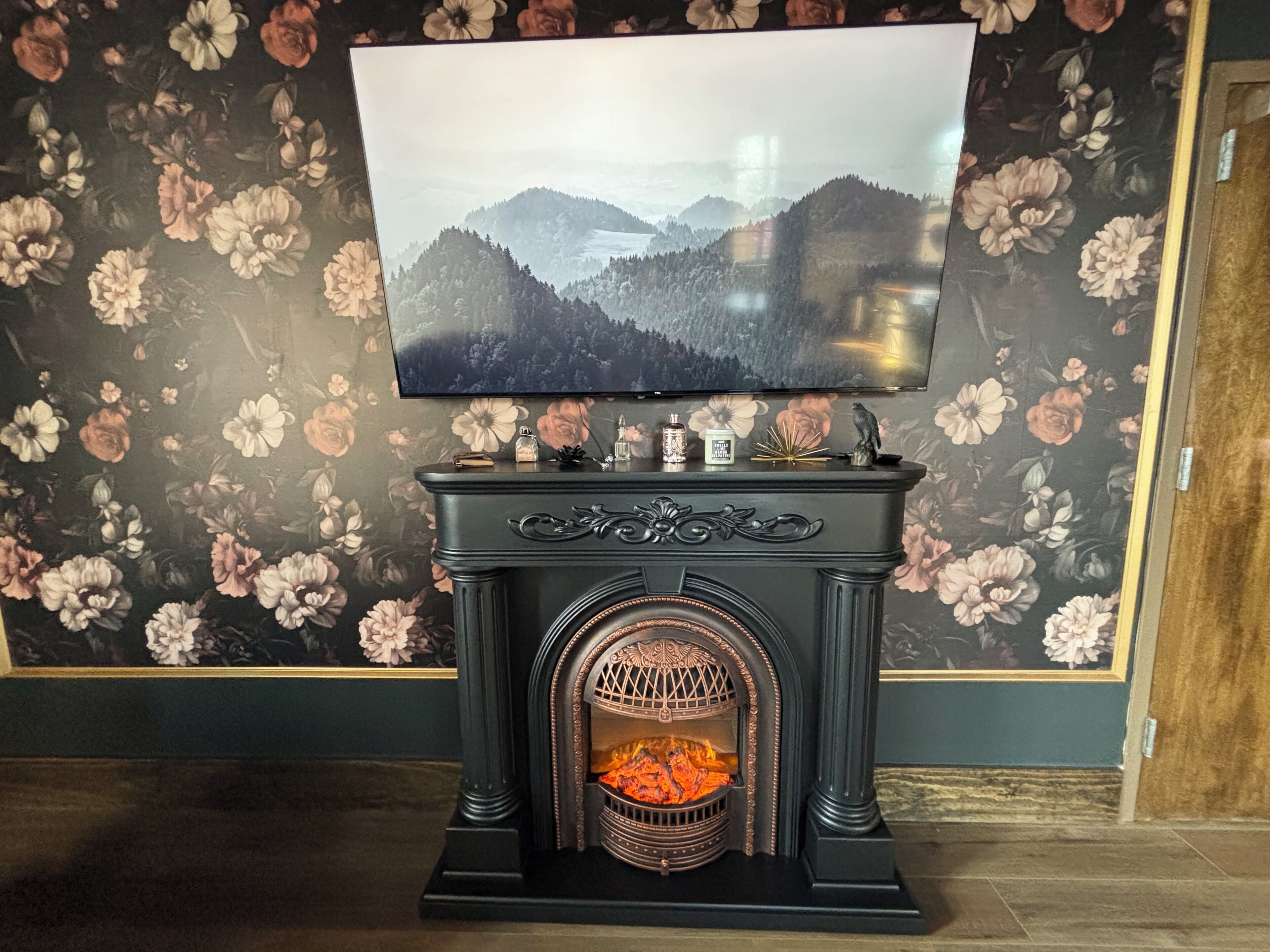 A fireplace with a television mounted above it, set against a floral wallpaper background.