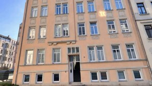 A multi-story building with a symmetrical facade, large windows, and a central entrance with a black door. - Modern 65m² apartment with parking space + balcony (Chemnitz)