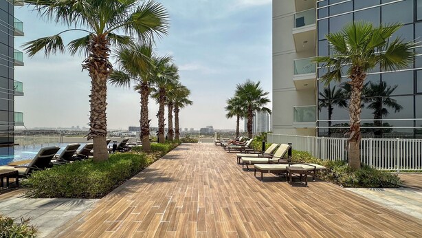 A rooftop lounge with sun loungers and palm trees, overlooking a cityscape. - Maison Privee - Refined Studio w/ Top Facilities in Damac Hills (Dubai)