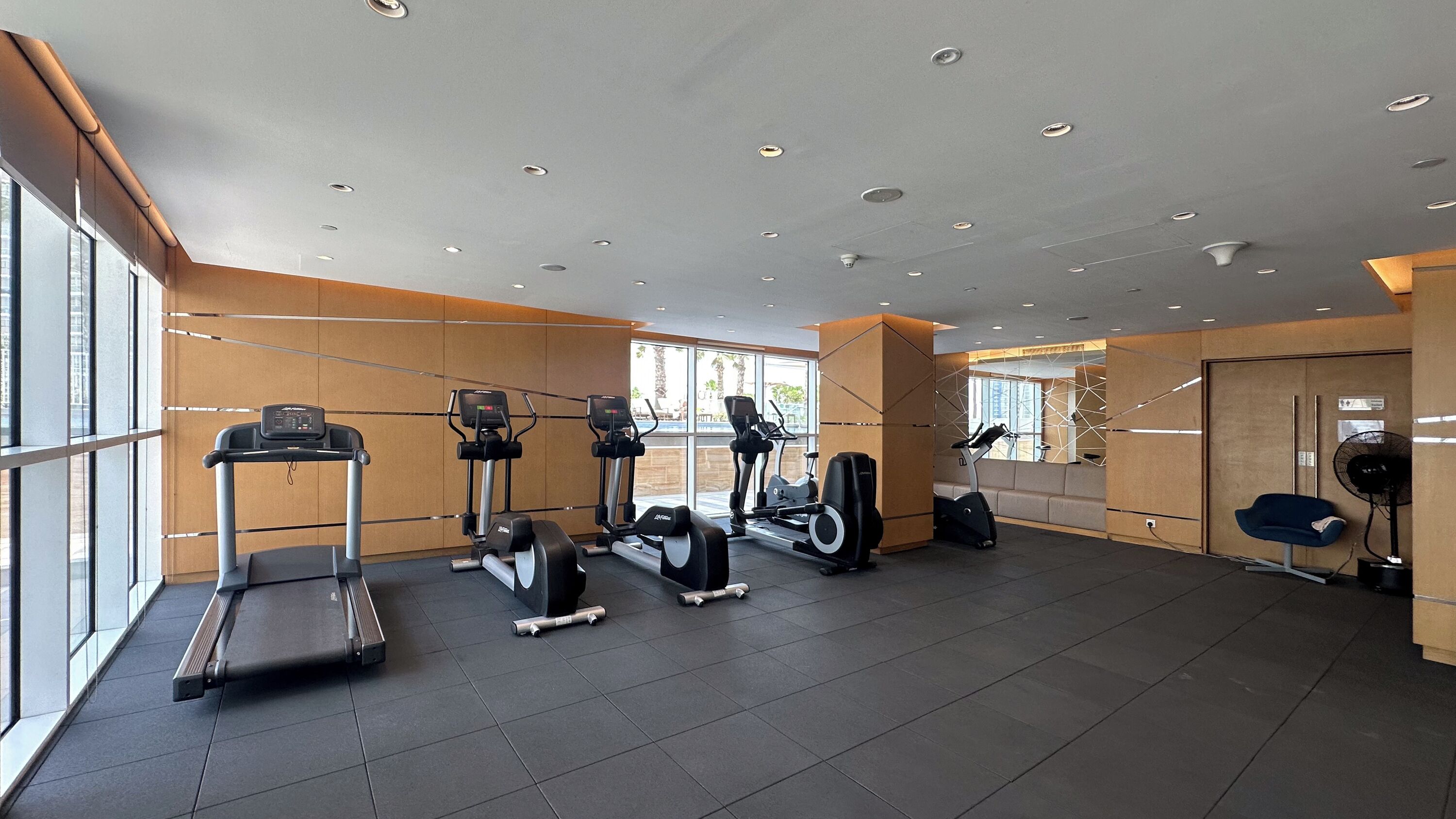 A modern gym with various cardio machines, a bench, and a fan.