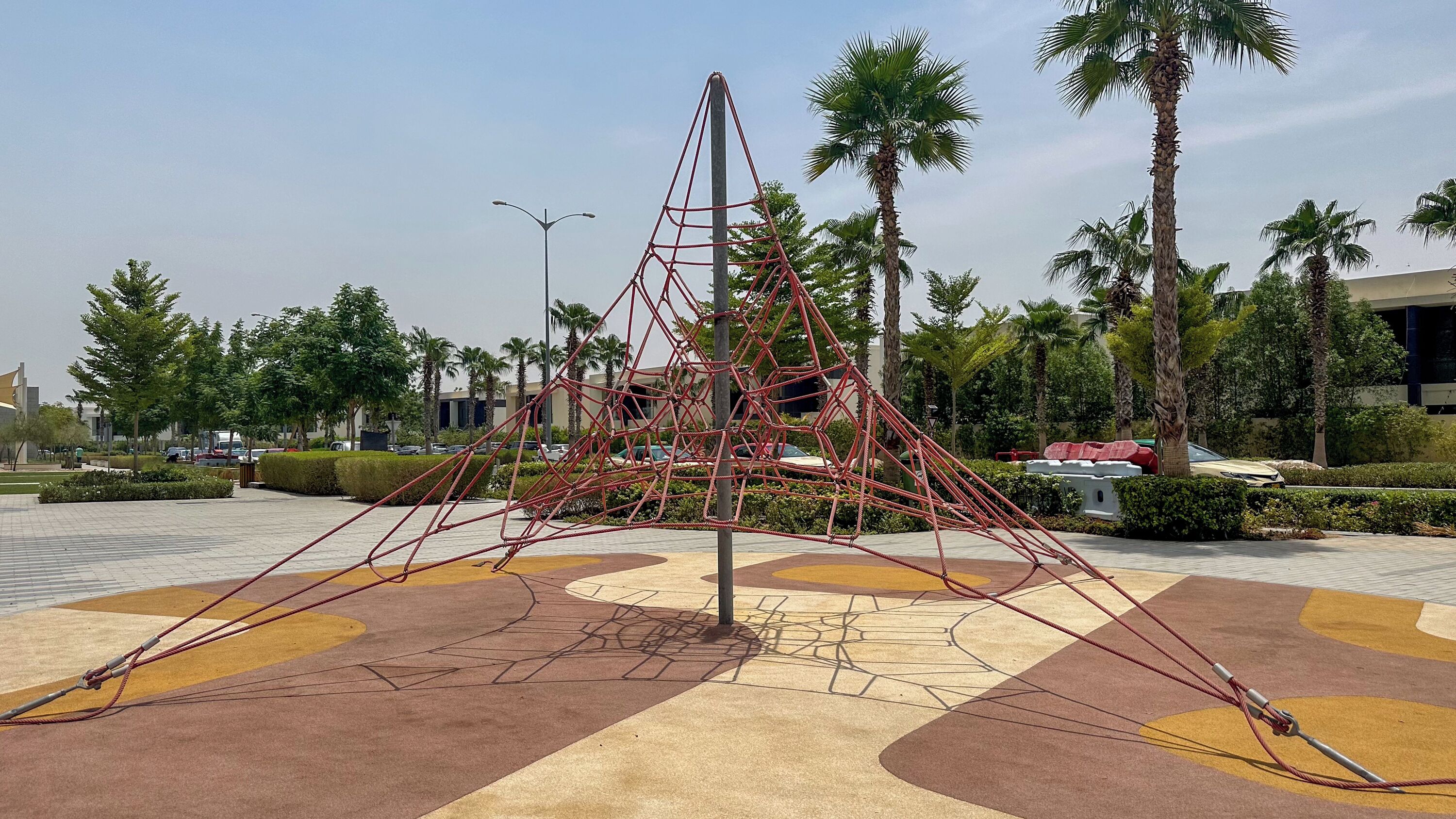 A geometric metal sculpture in a landscaped area with palm trees and a paved walkway.