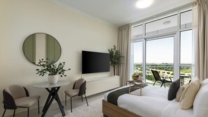 A modern hotel room with a large bed, a flat-screen TV, a dining table, and a view of the city. - Maison Privee - Refined Studio w/ Top Facilities in Damac Hills (Dubai)