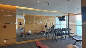 A gym with exercise equipment, a large mirror, and a view of the outside. - Maison Privee - Refined Studio w/ Top Facilities in Damac Hills (Dubai)