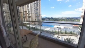 A balcony with a view of a river, a swimming pool, and high-rise buildings.
