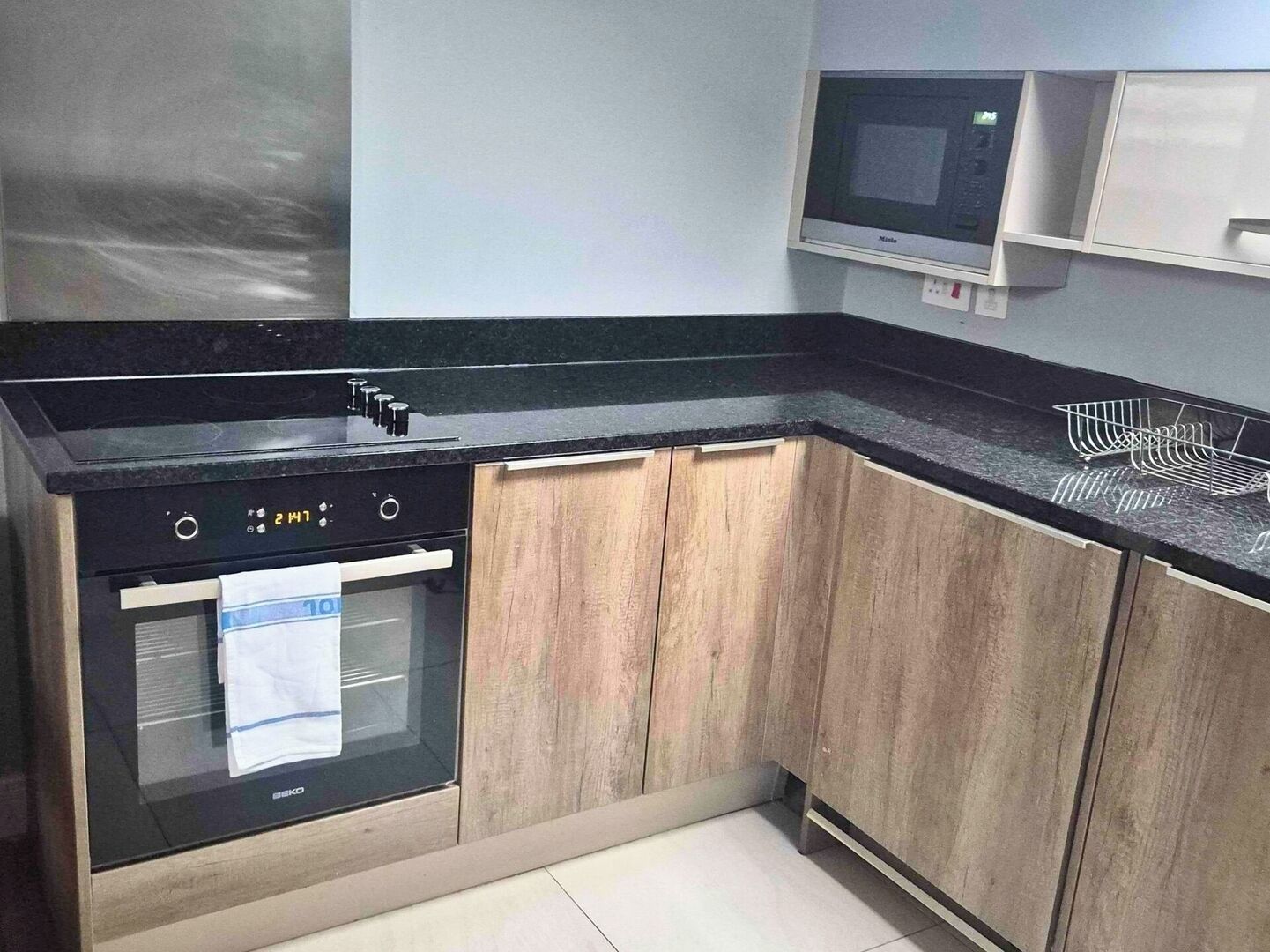Une cuisine moderne avec des meubles en bois, un plan de travail noir et un four à micro-ondes encastré.