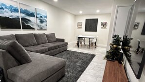 Ein modernes Wohnzimmer mit einer grauen Eckcouch, einem Holztisch und einem Essbereich mit weißem Tisch und Stühlen.