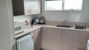 A compact kitchen with white cabinets, a microwave, a kettle, and a small refrigerator. - Charlies Motor Lodge (Balclutha)