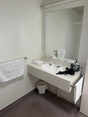 Un baño con un lavamanos blanco, un espejo y un perchero para toallas.